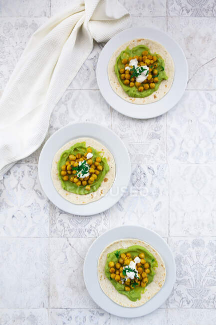 Plates of pita breads with mashed avocados, turmeric chick-peas,yogurtand parsley — Stock Photo