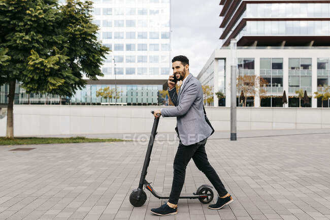 Jovem empresário casual com scooter elétrico falando ao telefone na cidade — Fotografia de Stock