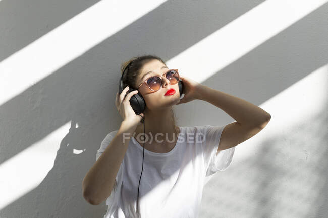 Портрет молодой женщины с красными губами, слушающей музыку в наушниках — стоковое фото