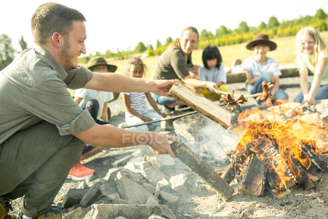 Вчитель готує вогнище для дітей, смажить ковбасу на паличках — стокове фото
