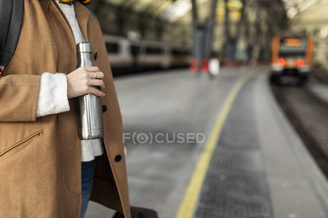 Gros plan de la femme tenant une fiole thermos à la gare — Photo de stock