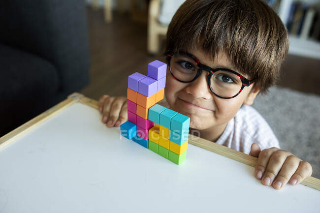 Retrato de niño sonriente con gafas jugando con bloques de construcción en casa - foto de stock