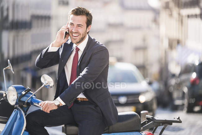 Jeune homme d'affaires riant avec scooter parlant au téléphone dans la ville, Lisbonne, Portugal — Photo de stock