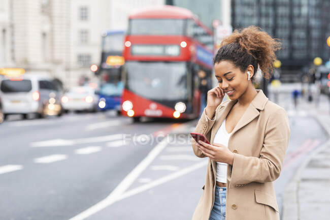 Giovane donna sorridente con cellulare e auricolari in città, Londra, Regno Unito — Foto stock