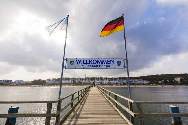 Germania, Meclemburgo-Pomerania occidentale, Heringsdorf, cartello di benvenuto appeso tra le bandiere nazionali sul molo di legno — Foto stock