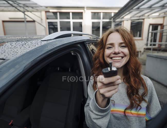 Portrait of happy redheaded woman beside car holding key — Stock Photo