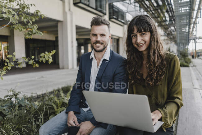 Portait de hombre de negocios sonriente y mujer de negocios casual utilizando el ordenador portátil al aire libre - foto de stock