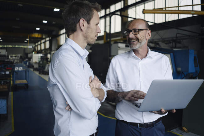 Dos hombres usando portátil en una fábrica - foto de stock