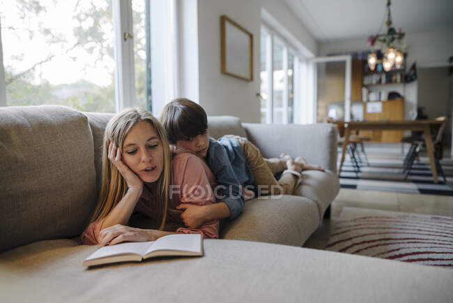Мать и сын лежат на диване, читая книгу — стоковое фото