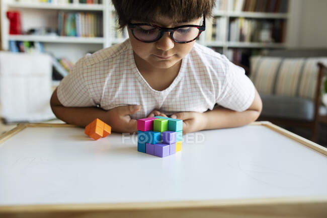 Niño pequeño con gafas jugando con bloques de construcción en casa - foto de stock