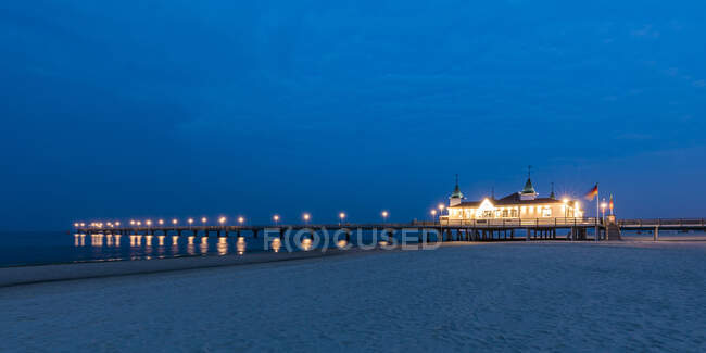 Germany, Mecklenburg-Western Pomerania, Heringsdorf, Sandy coastal beach at dusk with illuminated pier in background — Stock Photo