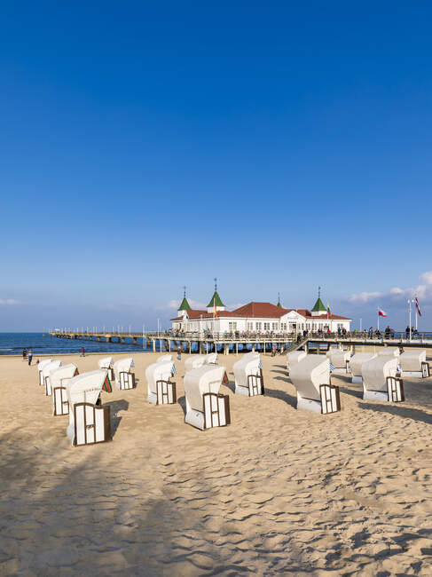 Germany, Mecklenburg-Western Pomerania, Heringsdorf, Hooded beach chairs on sandy coastal beach with pier in background — Stock Photo