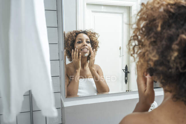Giovane donna in bagno applicare la crema viso — Foto stock