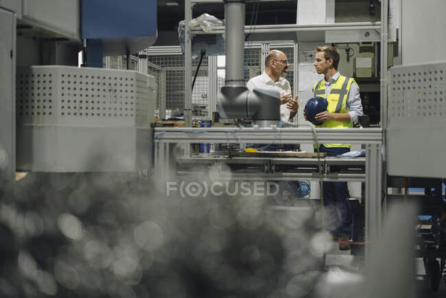 Businessman and man in reflective vest talking in a factory — Stock Photo