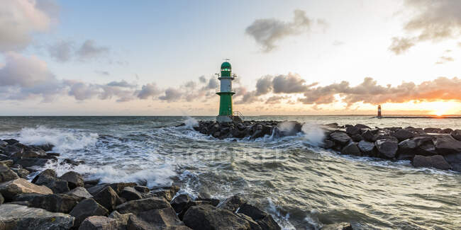 Germania, Meclemburgo-Pomerania occidentale, Warnemunde, Faro e onde marine che si infrangono contro le rocce al tramonto — Foto stock