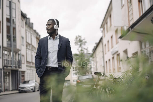 Jeune homme d'affaires écoutant de la musique avec écouteurs marchant dans la rue — Photo de stock