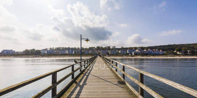 Germany, Mecklenburg-Western Pomerania, Heringsdorf, Diminishing perspective of wooden pier with town in background — Stock Photo