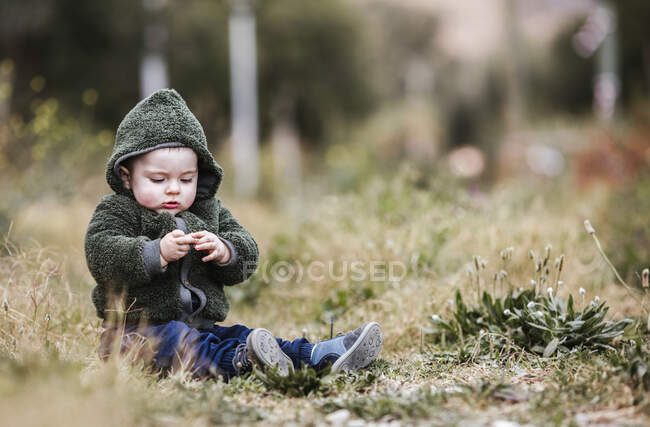 Portrait of little boy wearing green hooded jacket sitting on a meadow — Stock Photo