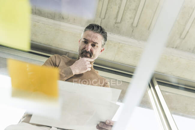 Зрілий бізнесмен працює над клею на скляному столі в офісі. — стокове фото
