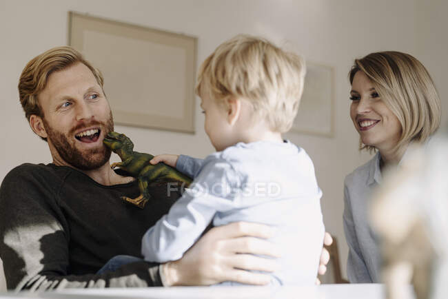 Família feliz brincando com figura de dinossauro em casa — Fotografia de Stock