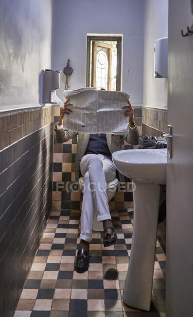 Stylish young businessman reading the newspaper sitting in the restroom — Stock Photo