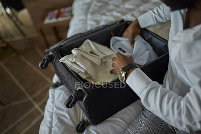 Empresario sentado en la cama en la habitación del hotel empacando su maleta - foto de stock
