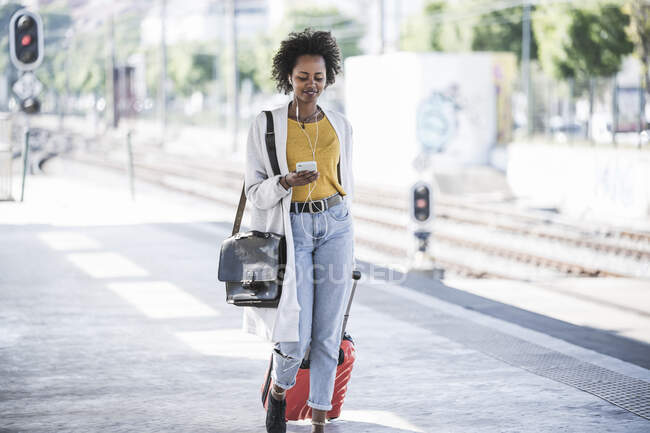 Giovane donna sorridente con cellulare e auricolari alla stazione ferroviaria — Foto stock
