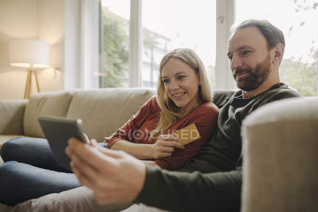 Пара сидить вдома на дивані, користуючись цифровим планшетом. — стокове фото