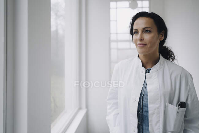 Médica mulher olhando pela janela, sorrindo — Fotografia de Stock