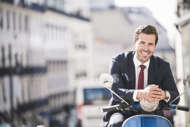 Portrait of smiling young businessman on motor scooter in the city, Lisbon, Portugal — Stock Photo