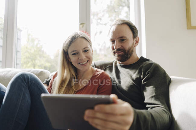 Casal sentado em casa no sofá, usando tablet digital — Fotografia de Stock