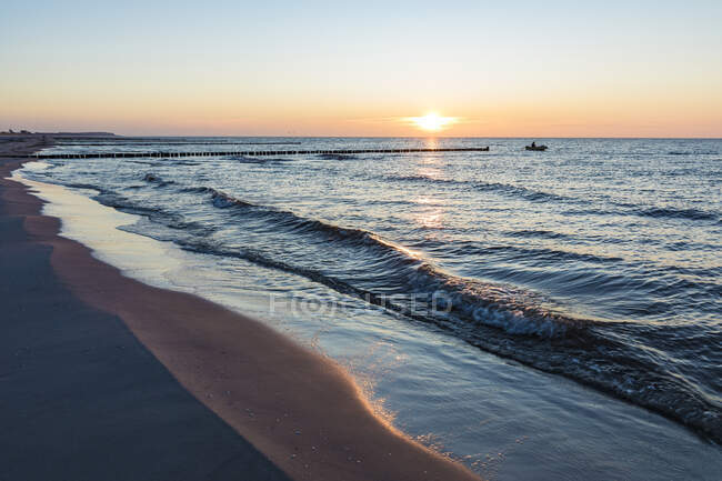 Germania, Meclemburgo-Pomerania occidentale, Vitte, Spiaggia costiera sabbiosa al tramonto con sagoma di peschereccio sullo sfondo — Foto stock