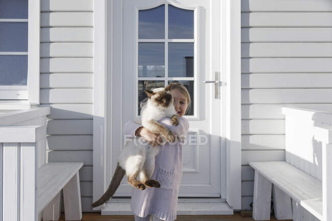 Little girl carrying cat on her arms in front of house entrance — Stock Photo