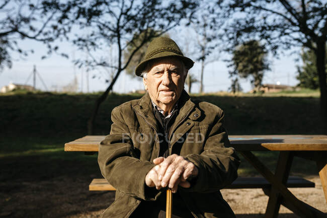 Alter Mann mit Stock sitzt auf Bankett in einem Park — Stockfoto