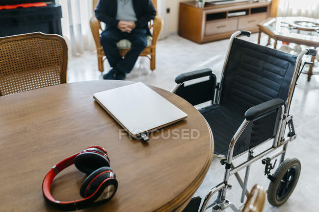 Auriculares y portátil con usb-stick en la mesa en la sala de estar del hombre mayor - foto de stock