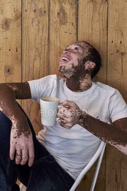 Jovem com vitiligo tendo uma xícara de café e rindo em uma cafetaria — Fotografia de Stock