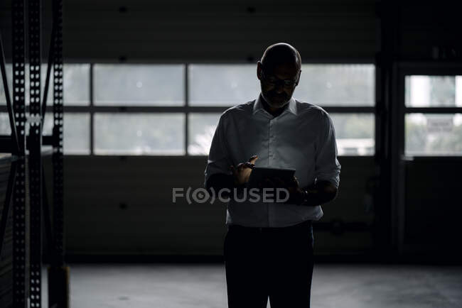 Geschäftsmann mit Tablet in einer Fabrik im Dunkeln — Stockfoto