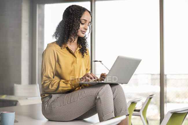 Joven mujer de negocios sentada en el escritorio en la oficina usando computadora portátil - foto de stock