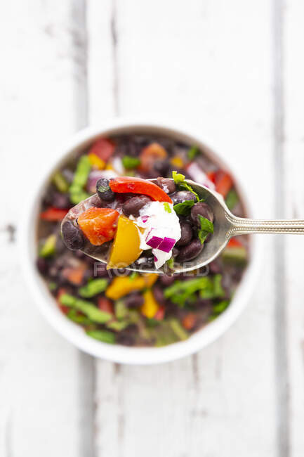 Spoon of black bean soup withbell pepper, cilantro, sour cream and red onions — Stock Photo