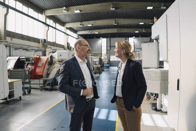 Glücklicher Geschäftsmann und Geschäftsfrau im Gespräch in einer Fabrik — Stockfoto