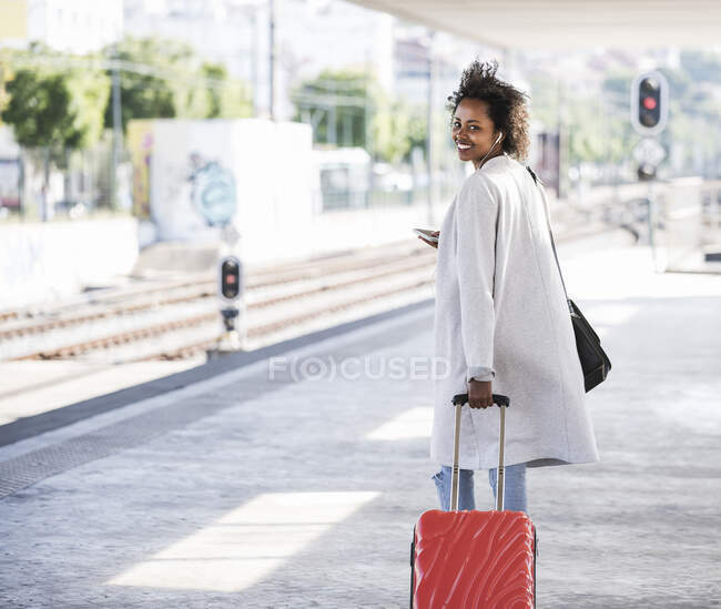 Giovane donna sorridente con valigia rotolante alla stazione ferroviaria — Foto stock
