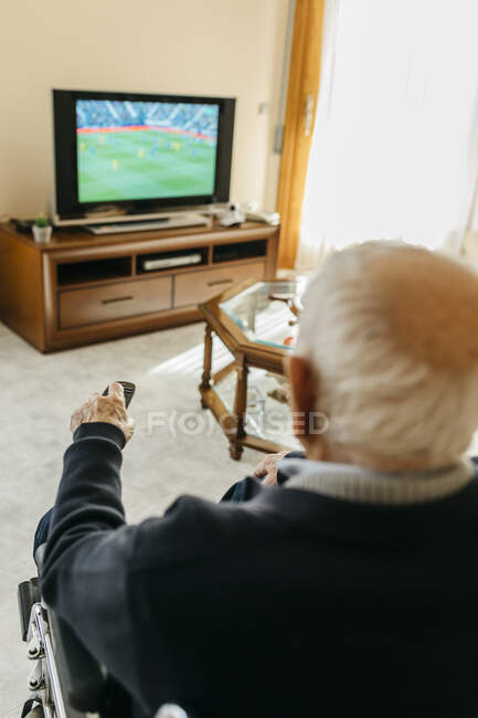 Зворотний бік дорослого чоловіка дивиться телевізор вдома, користуючись дистанційним контролем. — стокове фото