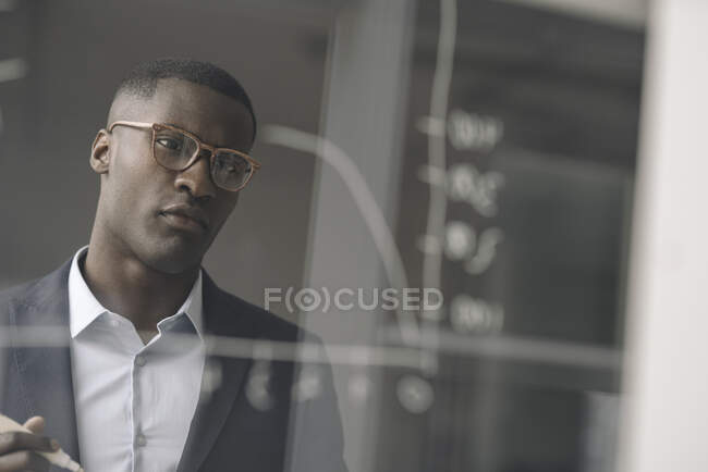 Porträt eines jungen Geschäftsmannes, der im Büro ein Diagramm auf einer Glasscheibe betrachtet — Stockfoto