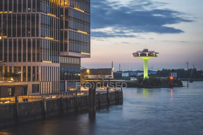 Germany, Hamburg,Waterfront building at dusk with Lighthouse Zero in background — Stock Photo