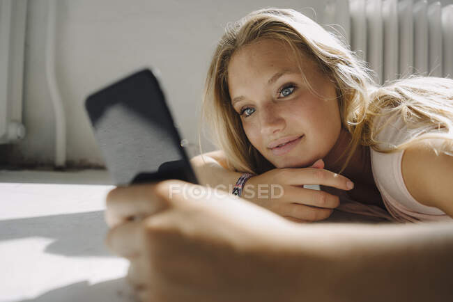 Mujer joven rubia acostada en el suelo usando el teléfono celular - foto de stock