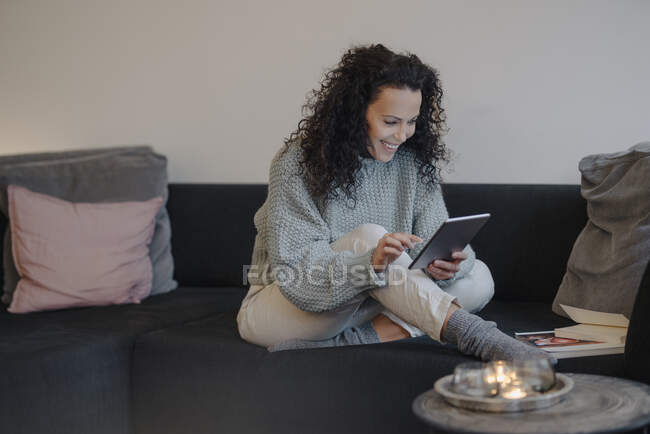 Femme assise à la maison sur le canapé, en utilisant une tablette numérique, lecture — Photo de stock