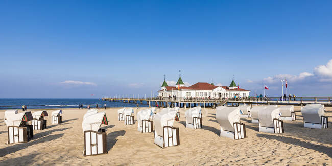 Germania, Meclemburgo-Pomerania occidentale, Heringsdorf, Sedie con cappuccio sulla spiaggia sabbiosa costiera con pontile sullo sfondo — Foto stock