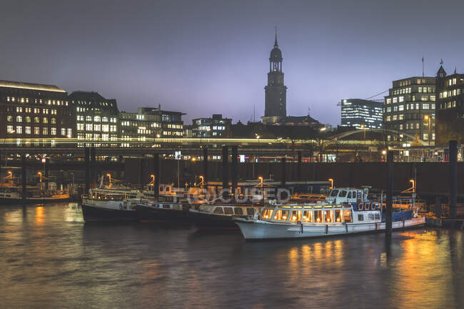Alemanha, Hamburgo, Barcos atracados no porto da cidade ao entardecer com luz trilha e torre da Igreja de Saint Michaels no fundo — Fotografia de Stock