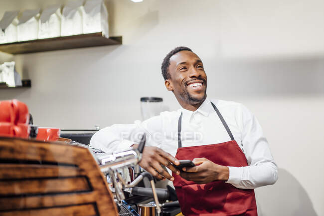 Felice barista che tiene il cellulare in una caffetteria — Foto stock