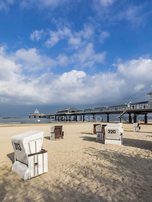 Germany, Mecklenburg-Western Pomerania, Heringsdorf, Clouds over hooded beach chairs on sandy coastal beach with pier in background — Stock Photo